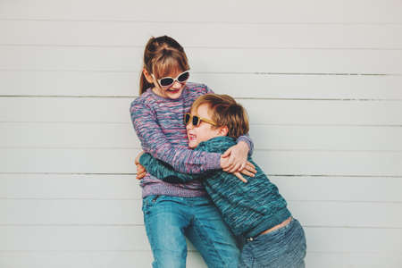 Group of two funny kids playing together outside, little boy and girl posing against white wooden background, brother and sister wearing matching pullovers, fashion for children, knitwear.の写真素材