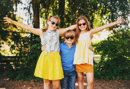 Outdoor portrait of 3 funny kids playing together in summer park. Happy childhoodの写真素材