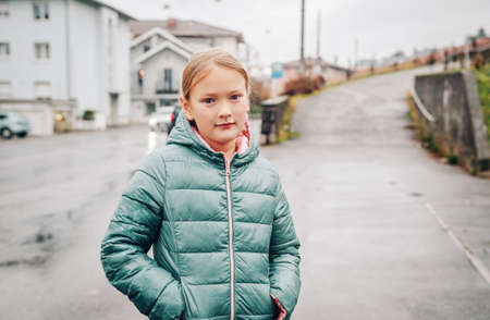 Outdoor portrait of pretty 8 year old girl on a rainy day, wearing green jacketの写真素材