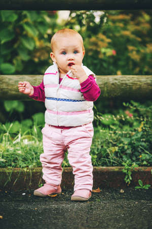Outdoor portrait of adorable baby girl of 9-12 months old playing in the park, wearing white...