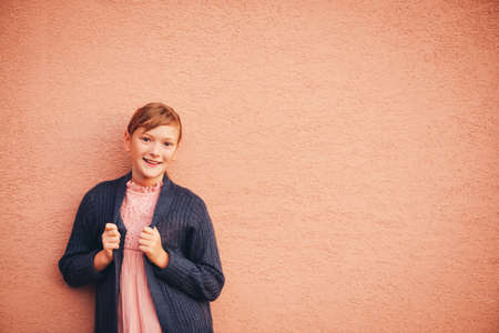 Outdoor portrait of adorable preteen girl wearing soft pink dress and purple cardigan, kid model...