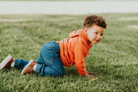 Adorable funny toddler playing outside, baby boy enjoying nice sunny day, 1-2 year old african kid crawling on the grass, film look toned imageの写真素材