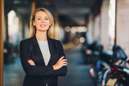 Portrait of beautiful blond woman on the street, wearing black jacket, arms crossedの写真素材