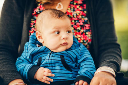 Adorable 3 months old baby holding by a mother resting in the park on a nice sunny dayの写真素材
