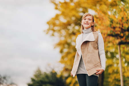 Autumn portrait of adorable preteen girl wearing leather jacket, posing against yellow tree