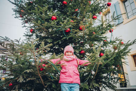 Happy little girl playing with Christmas tree on the streets of old european city, holiday travel with kids, image taken in Lausanne; Switzerlandの写真素材