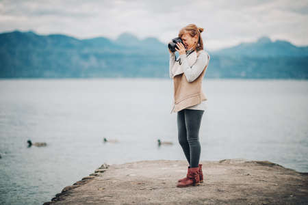 Cute little preteen girl enjoying nice day on lake Geneva, taking pictures with dslr camera, wearing beige jacket. Travel with children. Image taken in Lausanne; Switzerlandの写真素材