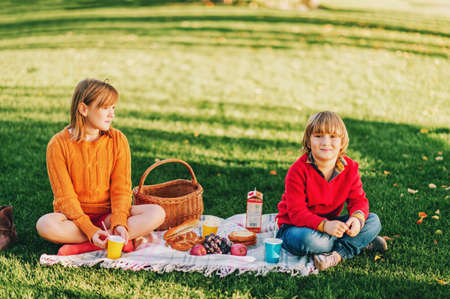 Kids eating snacks outside. Children resting in the park on a nice sunny day, sitting on the blanketの写真素材