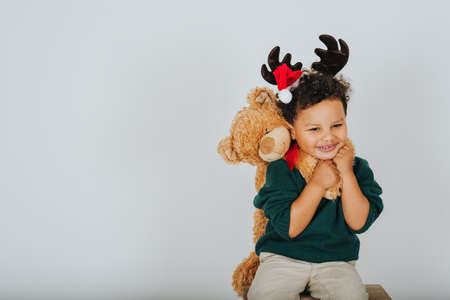Christmas portrait of adorable toddler boy wearing green pullover, reindeer ears with Santa Claus' hat, holding teddy bear の写真素材