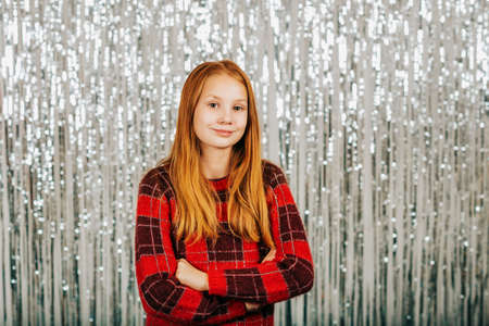 Christmas portrait of cute little girl against silver background, wearing red pullover, arms crossedの写真素材