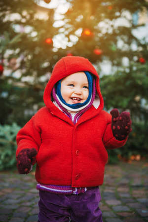 Outdoor portrait of sweet little 1 year old baby girl playing with Christmas tree, wearing red jacketの写真素材
