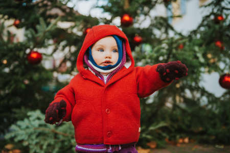Outdoor portrait of sweet little 1 year old baby girl playing with Christmas tree, wearing red jacketの写真素材