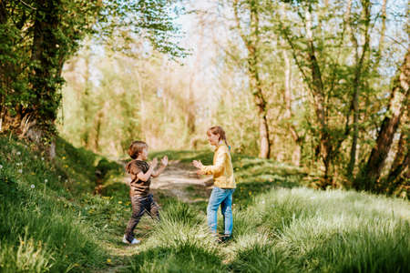 Two funny kids playing together in spring forest, little brother and sister enjoying nice walk in woodsの写真素材