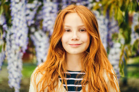 Close up portrait of adorable 9-10 year old red-haired kid girl posing in wisteriaの写真素材