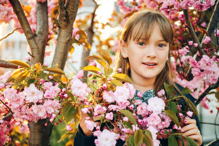 Outdoor spring portrait of a pretty little girl, standing between flowers of a japanese cherry in blossomの写真素材