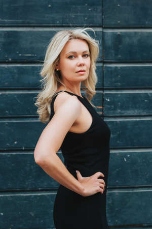 Outdoor portrait of young blond woman wearing black dress