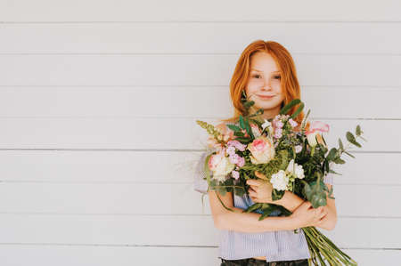 Close up portrait of adorable red hair kid girl holding big flower bouquet with rosesの写真素材