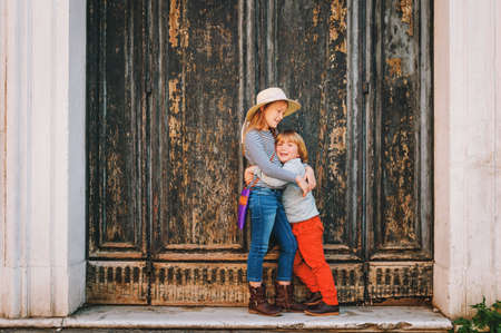 Outdoor portrait of cute little boy and girl, stylish kids posing against vintage old greem door. Fashion for small childrenの写真素材