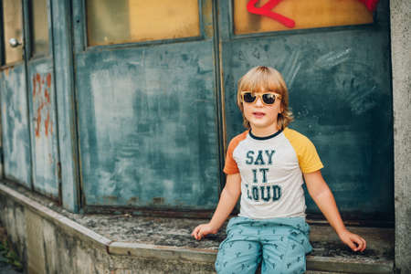 Outdoor portrait of funny little boy wearing sunglasses and t-shirt with sign "Say It Loud"の写真素材