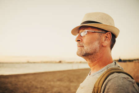 Handsome man on summer vacation by the sea, wearing hat, glasses and backpack