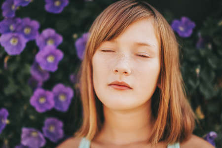Daydreaming pretty kid girl, close up portrait against purple flower wall. Eyes closedの写真素材