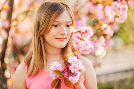 Spring portrait of young preteen kid girl with pink blooming flowersの写真素材