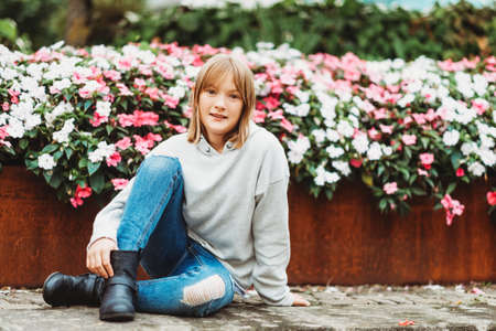 Outdoor portrait of funny little girl wearing grey sweatshirt, denim jeans and black boots