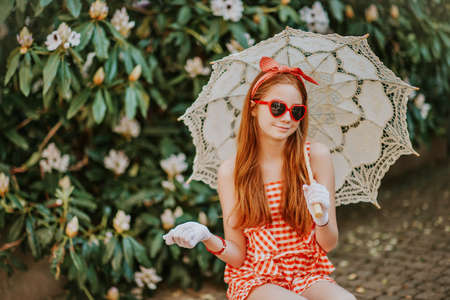 Funny little girl wearing gingham playsuit, heart shaped sunglasses, white gloves, holding lace parasol, retro stylized imageの写真素材