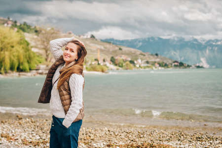Young happy woman enjoying nice spring day by Lake Geneva, Switzerland. Fashion girl wearing brown padded jacket and white pulloverの写真素材