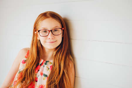 Portrait of adorable preteen kid girl of 10-11 yers old with long red hair, wearing eyeglasses
