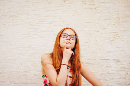 Portrait of adorable preteen kid girl of 10-11 yers old with long red hair, wearing eyeglasses