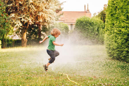 Child playing with garden sprinkler, jumping overの写真素材