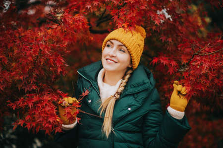 Autumn portrait of young beautiful woman wearing green jacket and set of yellow hat and gloves,...