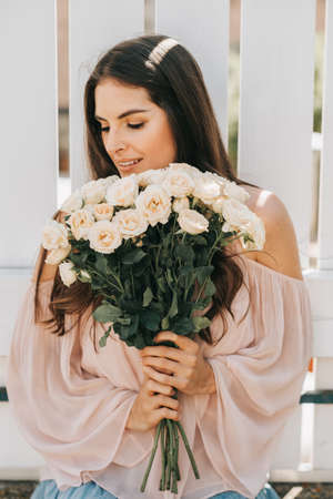 Happy beautiful woman with soft white roses, wearing blush cold shoulder blouseの写真素材