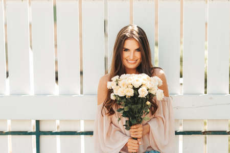 Happy beautiful woman with soft white roses, wearing blush cold shoulder blouseの写真素材