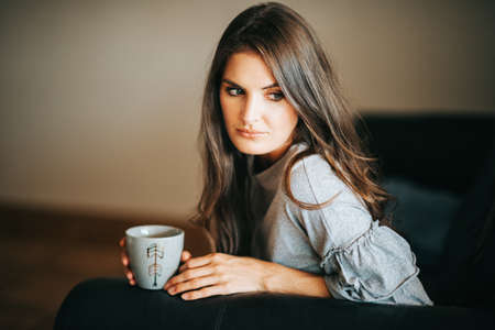 Young beautiful woman resting on the couch, holding cup of teaの写真素材