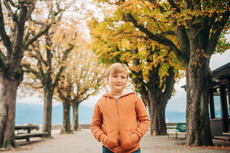 Cute little 7 year old boy posing in autumn park, wearing orange zip through hoody