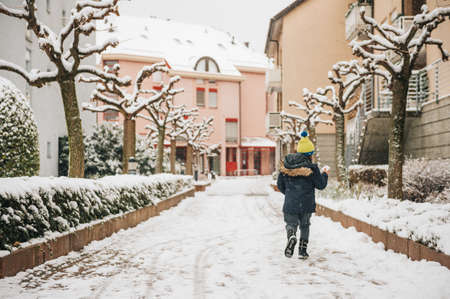 Outdoor portrait of funny little boy having fun under heavy snowfall