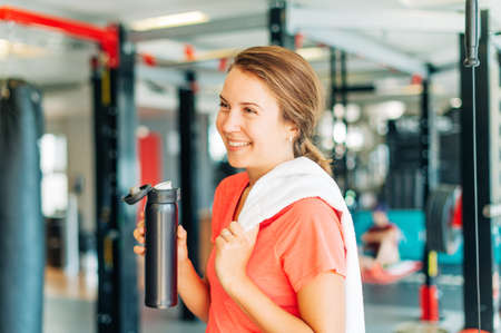 Happy and tired woman in sport gym, holding white towel and bottle of water
