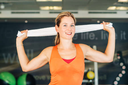 Happy and healthy woman in sport gym, holding white towel
