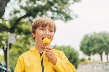 Cute little boy wearing yellow rain coat, eating mango ice creamの写真素材