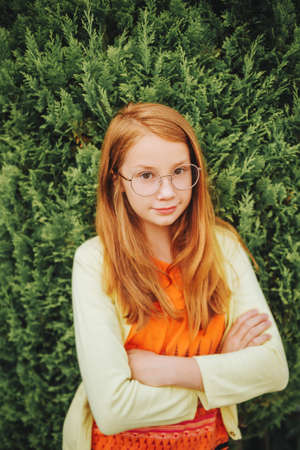 Portrait of adorable red-haired girl wearing glasses, arms crossed