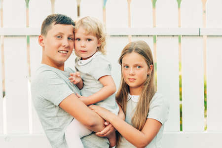 Group of 3 happy kids, family with teenage boy, little girl and toddler, hugs and love
