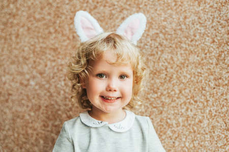 Portrait of adorable toddler girl with blonde curly hair wearing bunny earsの写真素材