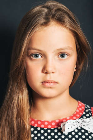 Studio shot of cute little girl wearing polkadot dress, posing on black background