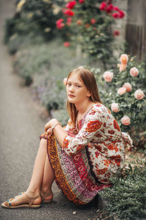 Summer portrait of pretty little girl wearing colorful dress, posing in rose gardenの写真素材
