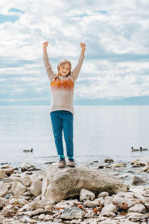 Funny little girl playing by the lake in early spring, wearing light pullover and blue chinos, fashion for young childrenの写真素材
