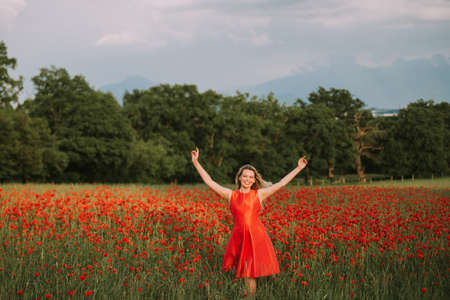 Beautiful woman enjoying nice day in poppy field, wearing red dress, arms wide openの写真素材