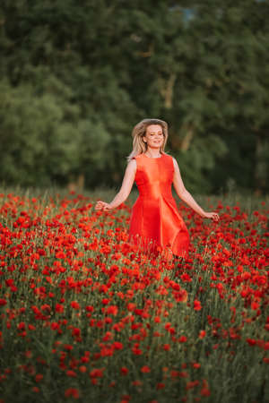 Beautiful woman enjoying nice day in poppy field, wearing red dressの写真素材