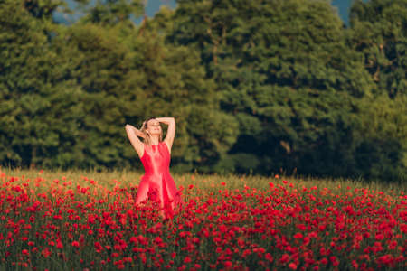 Beautiful woman enjoying nice day in poppy field, wearing red dressの写真素材